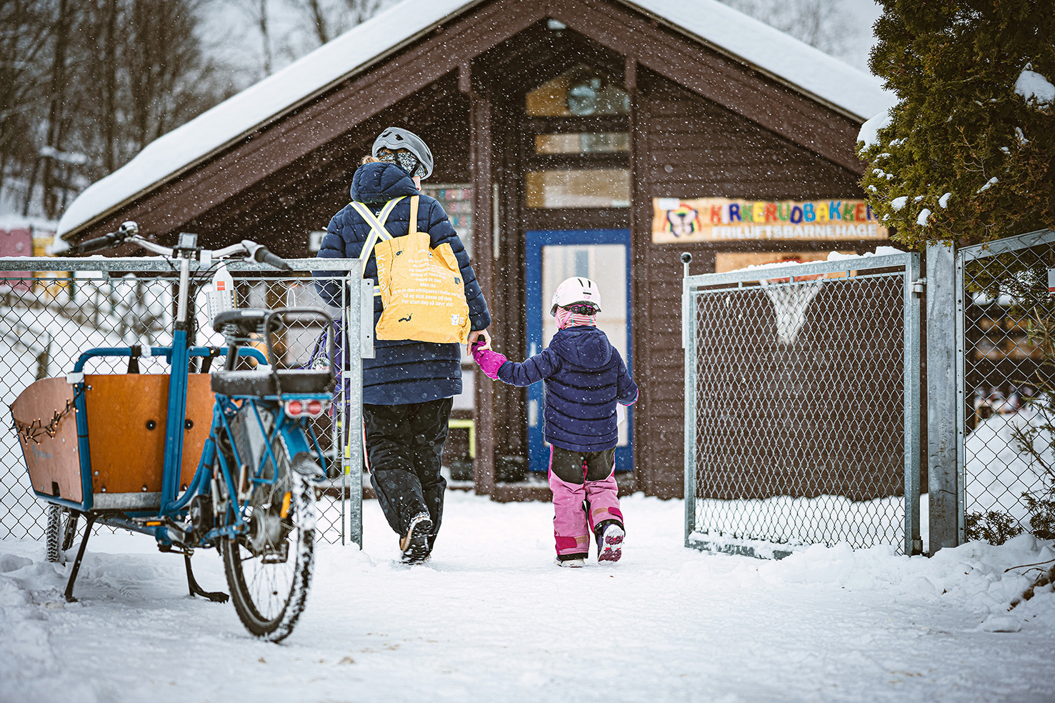 Bilde av voksen person og barn foran barnehage med sykkel