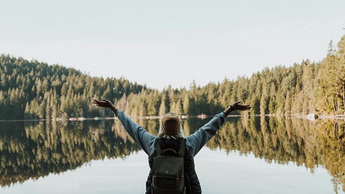 Dame strekker hendene opp mot en innsjø